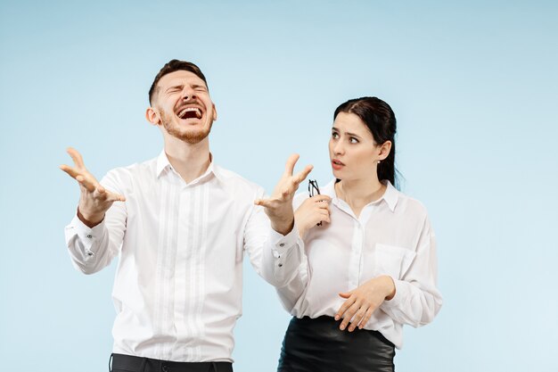 Giovani coppie felici emozionanti che esaminano macchina fotografica con gioia. Uomo d'affari e donna isolata su sfondo blu studio