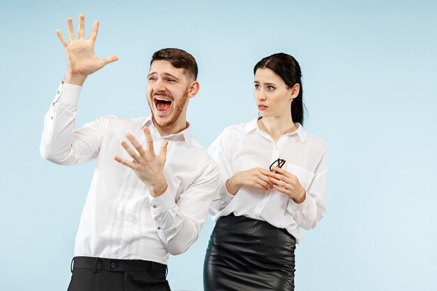 Giovani coppie felici emozionanti che esaminano macchina fotografica con gioia. Uomo d'affari e donna isolata su sfondo blu studio