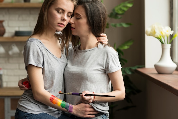 Giovani coppie lesbiche amorose con il pennello e la bandiera dipinta dell&#39;arcobaleno a disposizione