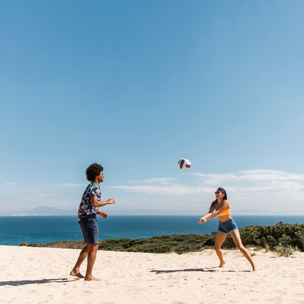 Giovani coppie multiculturali che giocano pallavolo sulla spiaggia