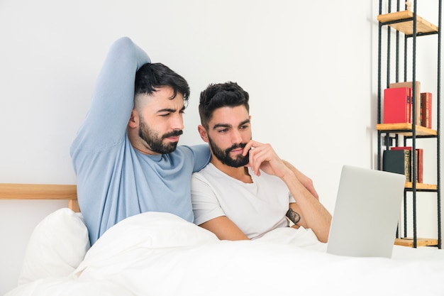 Giovani coppie premurose che si siedono sul letto che esamina computer portatile