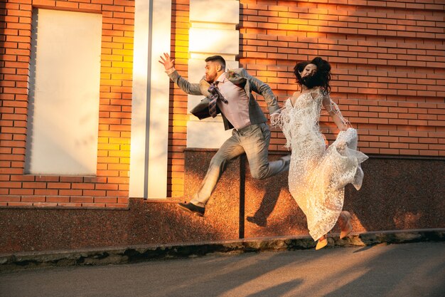 Giovani coppie romantiche caucasiche che celebrano il matrimonio in città. Tenera sposa e sposo sulla strada della città moderna. Famiglia, relazione, concetto di amore