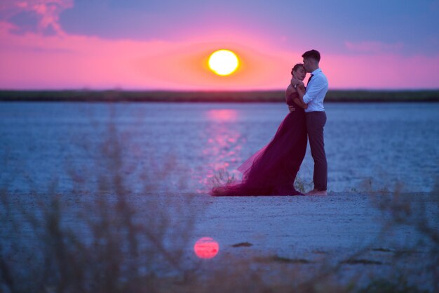 Giovani coppie romantiche che si rilassano sulla spiaggia che guarda il tramonto