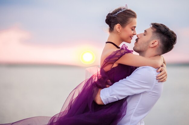 Giovani coppie romantiche che si rilassano sulla spiaggia che guarda il tramonto