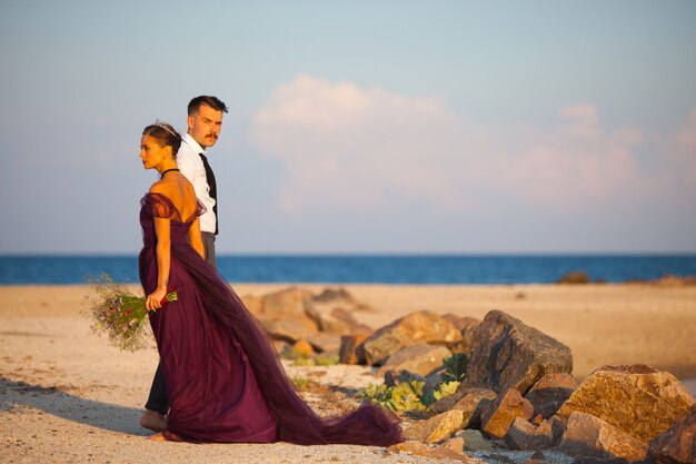 Giovani coppie romantiche che si rilassano sulla spiaggia che guarda il tramonto