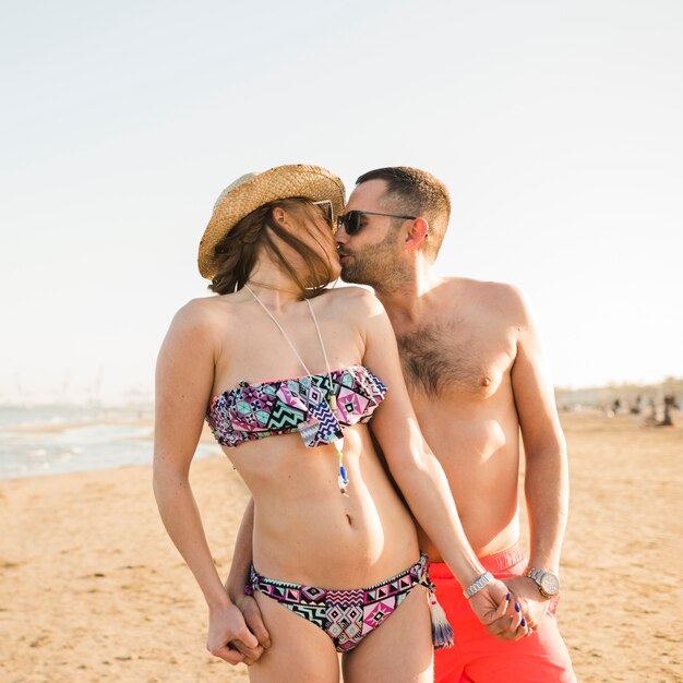 Giovani coppie romantiche che tengono la mano di ciascuno che bacia alla spiaggia