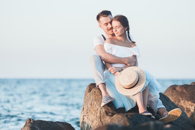 Giovani coppie romantiche felici che si rilassano sulla spiaggia e che guardano il tramonto