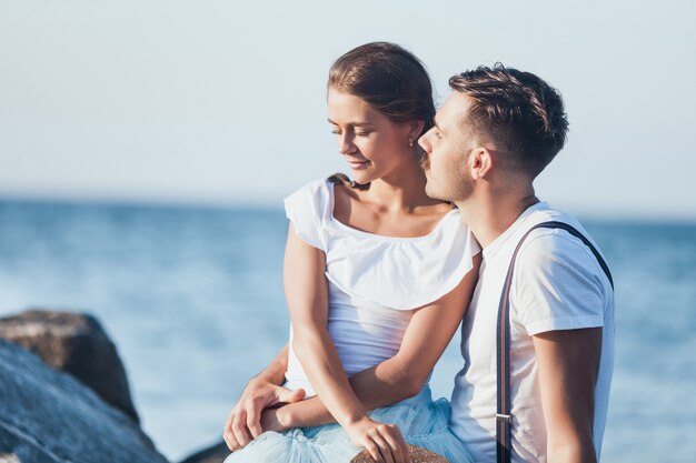 Giovani coppie romantiche felici che si rilassano sulla spiaggia e che guardano il tramonto