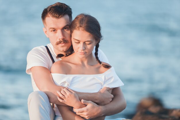 Giovani coppie romantiche felici che si rilassano sulla spiaggia e che guardano il tramonto