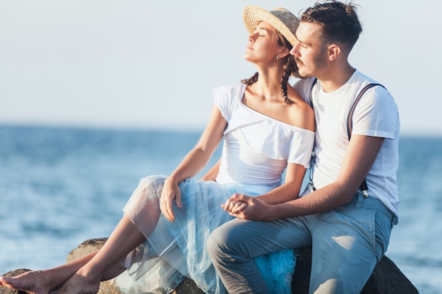 Giovani coppie romantiche felici che si rilassano sulla spiaggia e che guardano il tramonto