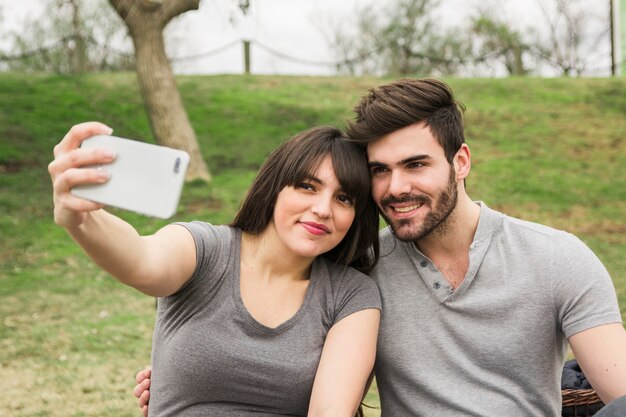 Giovani coppie sorridenti che prendono autoritratto sul telefono cellulare nel parco