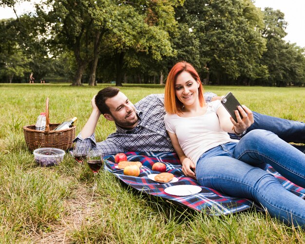 Giovani coppie sorridenti che prendono selfie nel picnic
