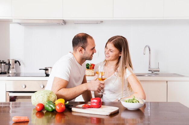 Giovani coppie sorridenti che tengono i bicchieri di vino che se lo esaminano