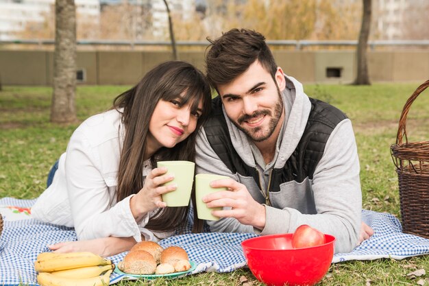 Giovani coppie sorridenti che tengono i vetri nel picnic al parco