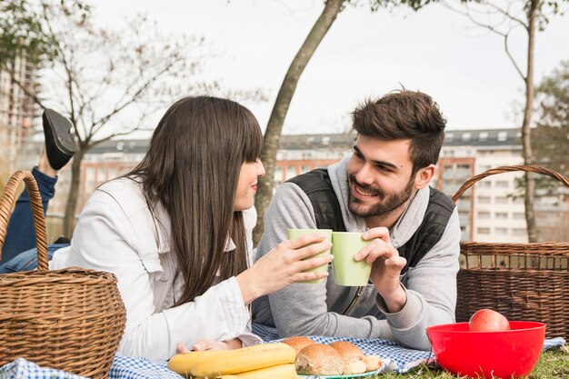 Giovani coppie sorridenti che tostano i vetri con alimento fresco al picnic