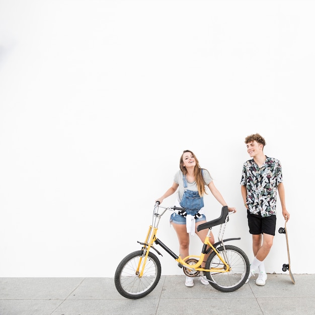 Giovani coppie sorridenti con la bicicletta e pattino contro la parete
