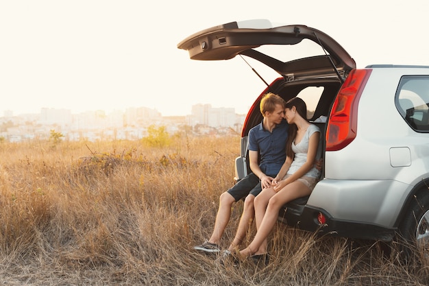 Giovani coppie sveglie nell'amore che si siede in un'automobile con un tronco aperto