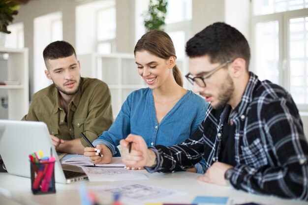 Giovani creativi con laptop che lavorano insieme su un nuovo progetto Gruppo di ragazzi sorridenti che trascorrono del tempo in un ufficio moderno