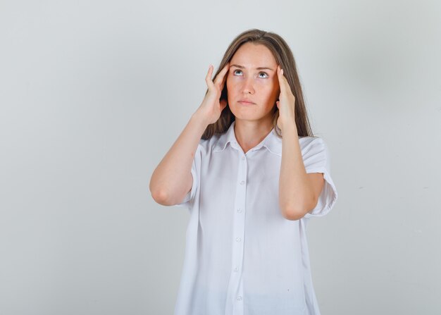 Giovani donne che soffrono di mal di testa in camicia bianca e che sembrano stanchi