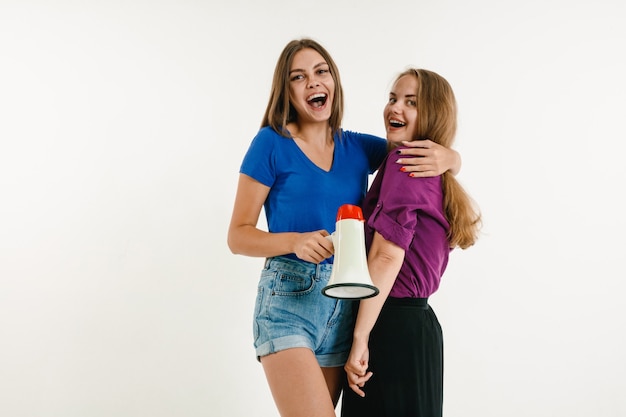 Giovani donne indossate nei colori della bandiera LGBT sul muro bianco. modelli in camicie luminose