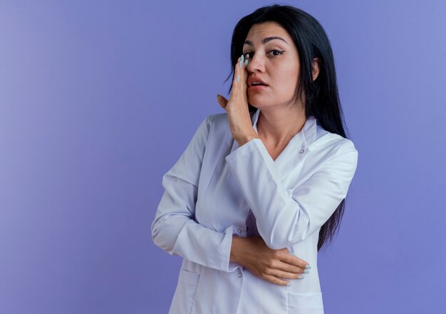 Giovani donne medico indossando accappatoio medico guardando tenendo la mano vicino alla bocca sussurrando,