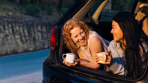 Giovani donne multietniche sorridenti che parlano nel tronco di automobile aperto