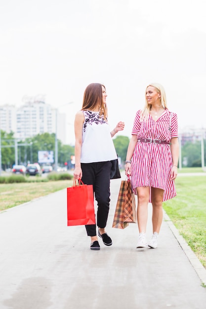 Giovani donne sorridenti che camminano con il sacchetto della spesa variopinto