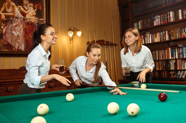 Giovani donne sorridenti che giocano a biliardo in ufficio oa casa dopo il lavoro.