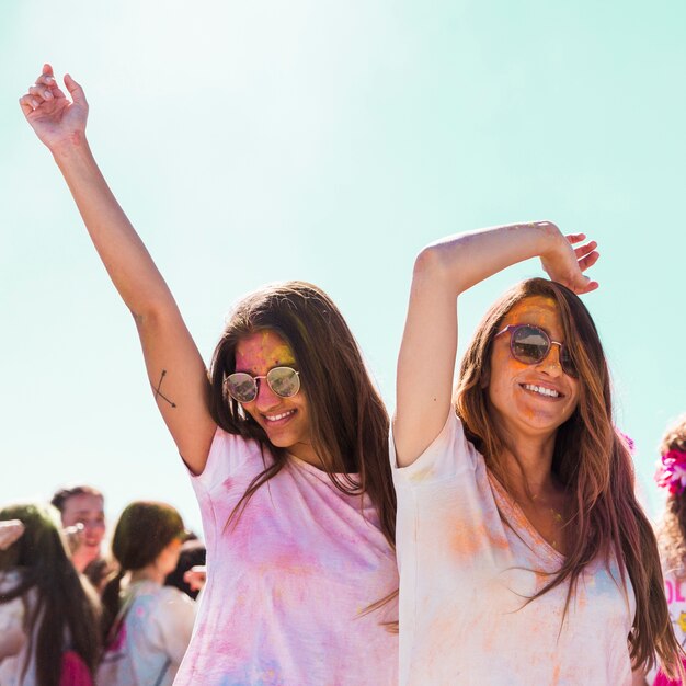 Giovani donne sorridenti che indossano gli occhiali da sole che ballano al festival di holi