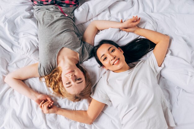 Giovani donne sorridenti che si trovano a letto e che si tengono per mano