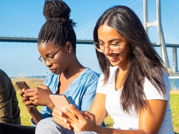 Giovani donne sorridenti che utilizzano gli smartphones nel parco