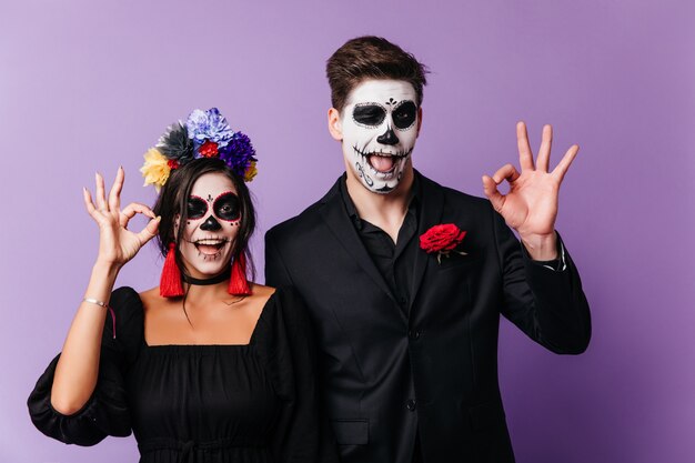 Giovani europei divertenti che scherzano a halloween. Tiro al coperto di ridere coppia di innamorati in abiti da zombie.