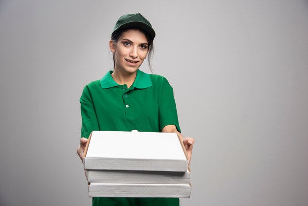 Giovani femmine corriere regalando scatole per pizza su sfondo grigio.