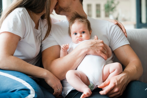 Giovani genitori che si baciano e che abbracciano il bambino a casa