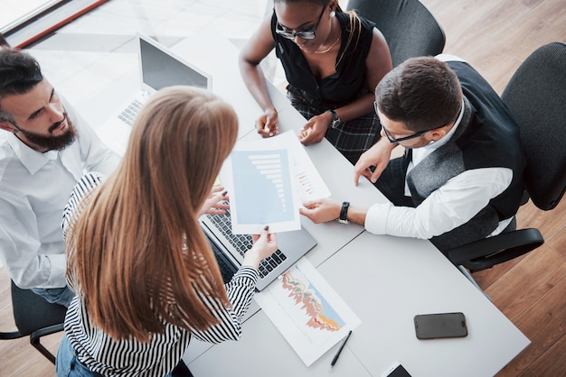 Giovani impiegati che si siedono nell'ufficio alla tavola e che per mezzo di un computer portatile, un concetto di riunione di "brainstorming" del lavoro di gruppo.