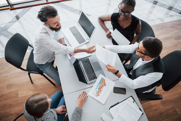 Giovani impiegati che si siedono nell'ufficio alla tavola e che per mezzo di un computer portatile, un concetto di riunione di "brainstorming" del lavoro di gruppo.