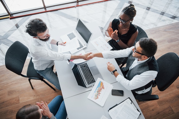 Giovani impiegati che si siedono nell'ufficio alla tavola e che per mezzo di un computer portatile, un concetto di riunione di "brainstorming" del lavoro di gruppo.