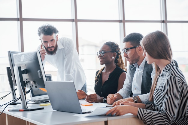 Giovani impiegati che si siedono nell'ufficio alla tavola e che per mezzo di un computer portatile, un concetto di riunione di "brainstorming" del lavoro di gruppo.