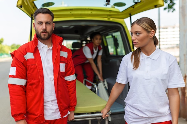 Giovani paramedici che spostano la barella dell'ambulanza dall'auto Paramedici in uniforme che prendono la barella fuori dall'auto dell'ambulanza