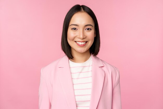 Giovani professionisti La commessa asiatica sorridente della donna di affari in vestito che guarda fiduciosa alla macchina fotografica che posa contro lo sfondo rosa