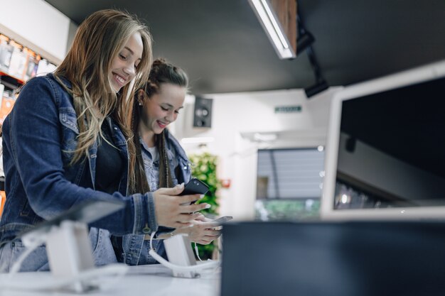 Giovani ragazze attraenti nei telefoni di prova del negozio di elettronica su una finestra del negozio. concetto di acquisto di gadget.