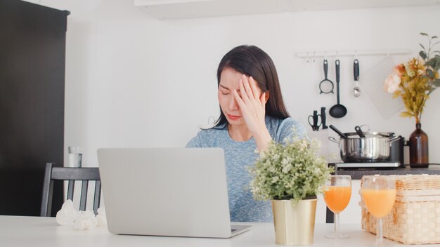 Giovani record asiatici della donna di affari di entrate e spese a casa. Signora preoccupata, seria, stress durante l'utilizzo del budget record del laptop, fiscale, documento finanziario che lavora nella cucina moderna a casa.