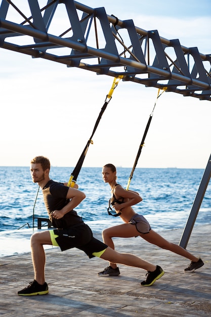 Giovani sportivi che si allenano con trx vicino al mare al mattino.