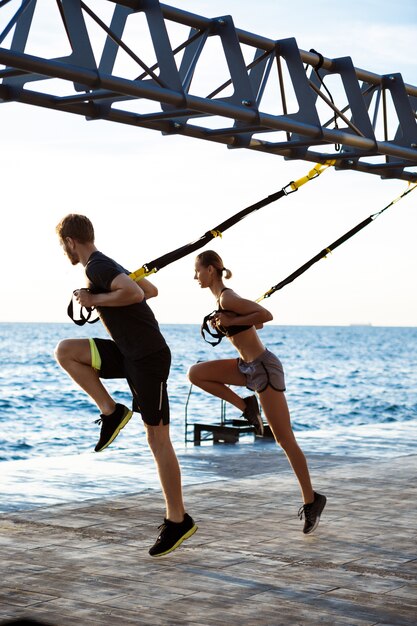 Giovani sportivi che si allenano con trx vicino al mare al mattino.