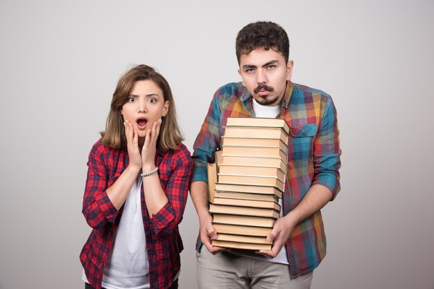 Giovani studenti che sembrano sorpresi e che tengono libri su sfondo grigio.