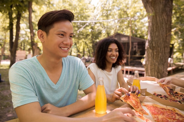 Giovani studenti multietnici sorridenti degli amici all'aperto che bevono succo che mangia pizza.