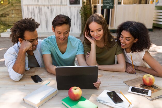 Giovani studenti multietnici sorridenti degli amici all'aperto facendo uso della compressa