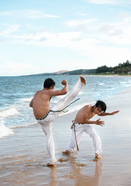 Giovani uomini senza camicia che praticano la capoeira insieme sulla spiaggia