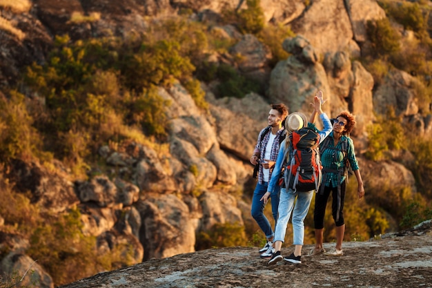 Giovani viaggiatori con zaini che sorridono, dando il cinque, camminando nel canyon