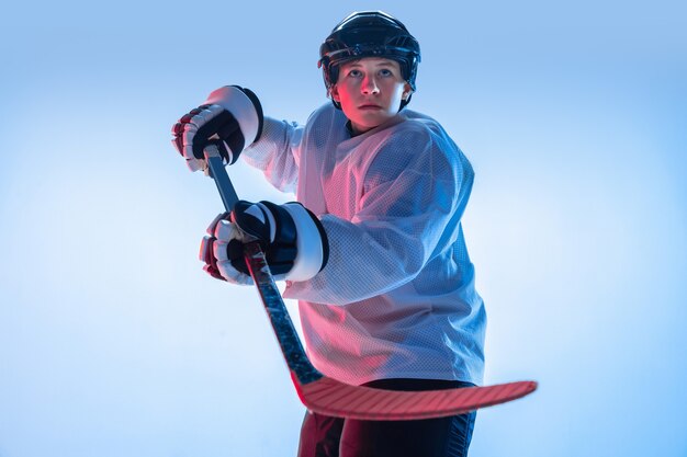 Gioventù. Giovane giocatore di hockey maschio con il bastone su sfondo bianco alla luce al neon. Sportivo che indossa attrezzatura e casco che pratica. Concetto di sport, stile di vita sano, movimento, movimento, azione.